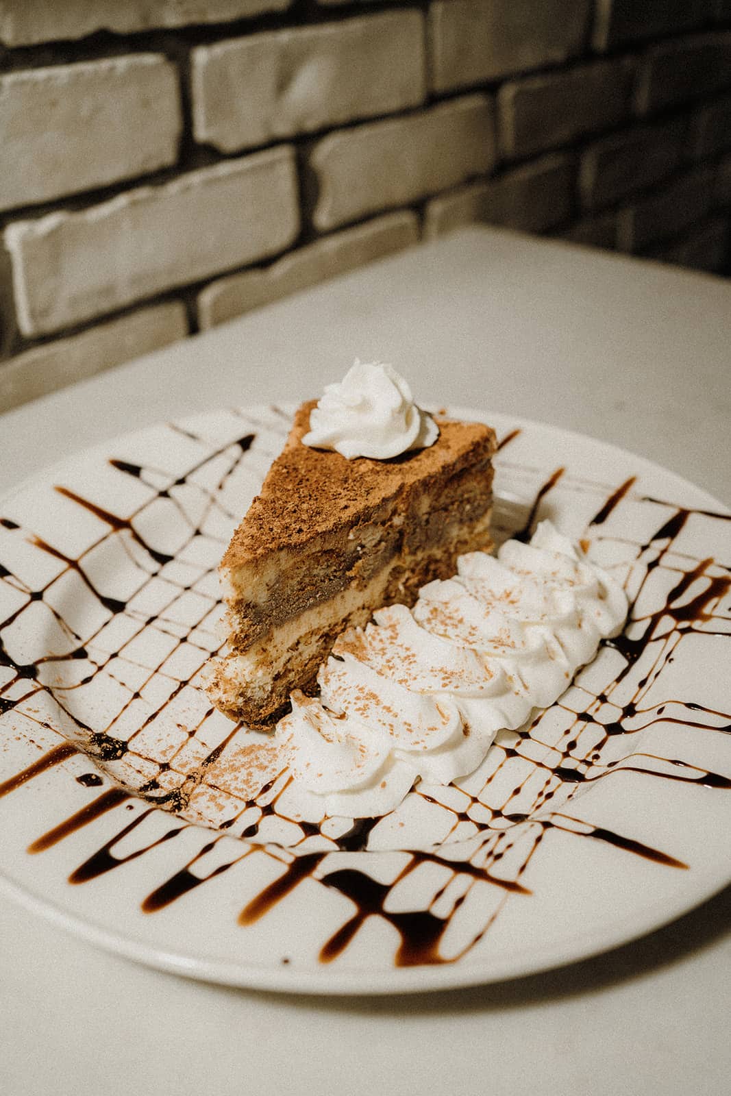 A slice of layered cake topped with whipped cream, served on a plate with chocolate drizzle and extra whipped cream.