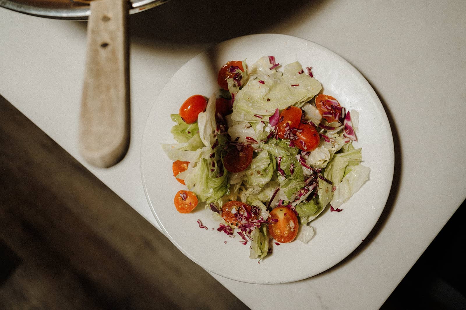 A plate of salad with lettuce, cherry tomatoes, and shredded red cabbage on a white surface.